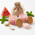 Pink Melon Lip Set with two 2oz glass jars open, burlap bag, lip scrubber brush, spoon and sponge, fresh watermelon slice and mint leaves on white background