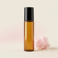 Pink Sugar roll-on body oil in a blank slender amber glass bottle with a black cap and sweet pink scent-inspired props